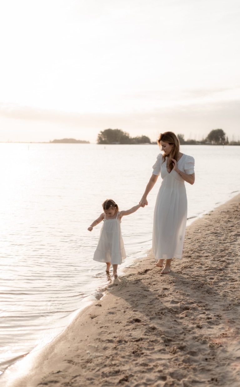 Motherhood liefdevolle shoot Twee meisjes lopen samen op het strand, omarmend met een zonsondergang op de achtergrond.