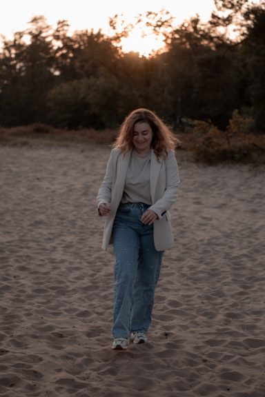 lifestyle shoot, golden hour, krachtige vrouw Vrouw met krullend haar in een zandige omgeving, loopt richting de camera bij zonsondergang.